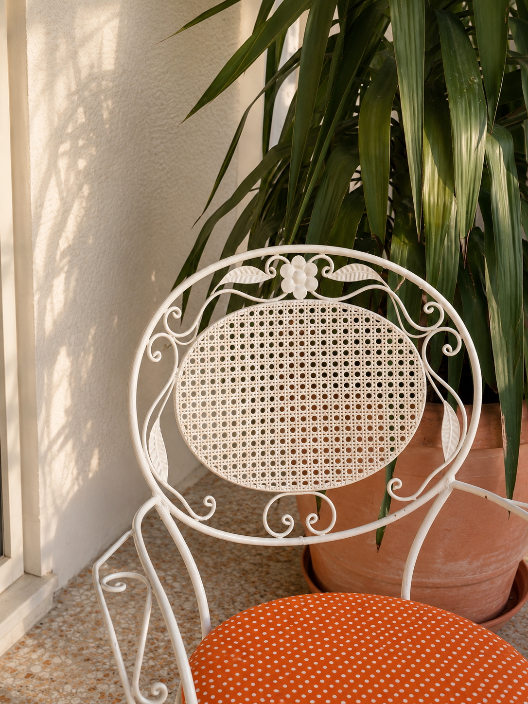 Vintage white terrace chair with woven back and orange dotted cushion