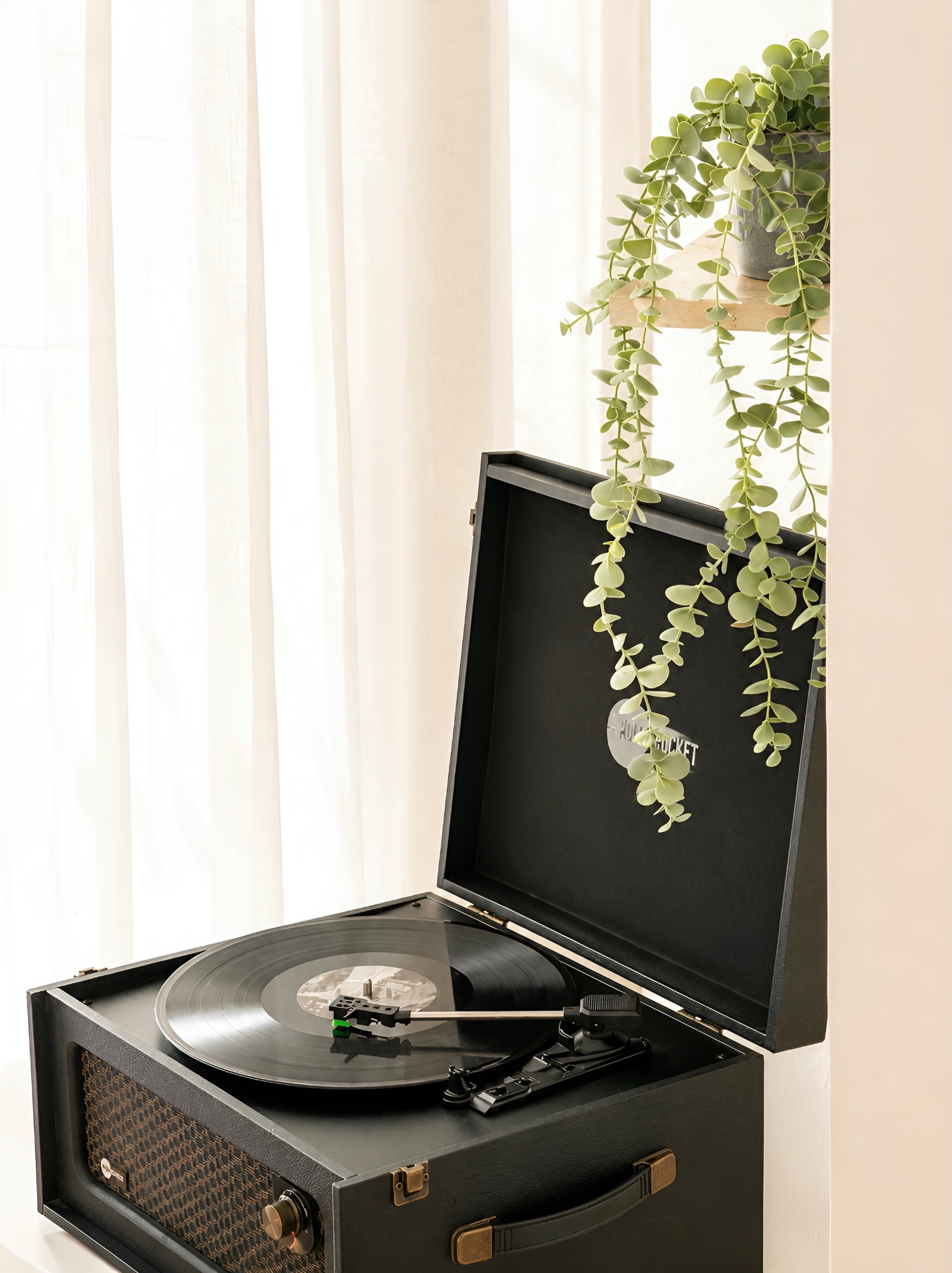 Vintage record player with trailing eucalyptus by sheer curtains