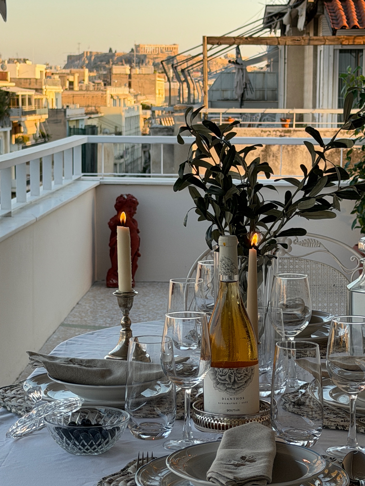 Candlelit terrace table set for dinner with olive branches and Acropolis view at sunset