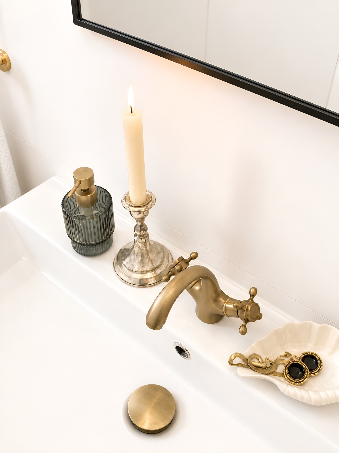 Candlelit vanity detail with brass tap and smoky glass dispenser
